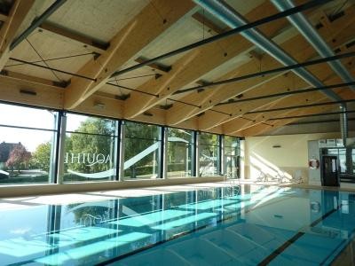 Innenansicht Hallenbad mit Schwimmbecken und Holzdeckenkonstruktion.