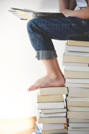 Kind das auf einem Bücherstapel sitzt und liest.