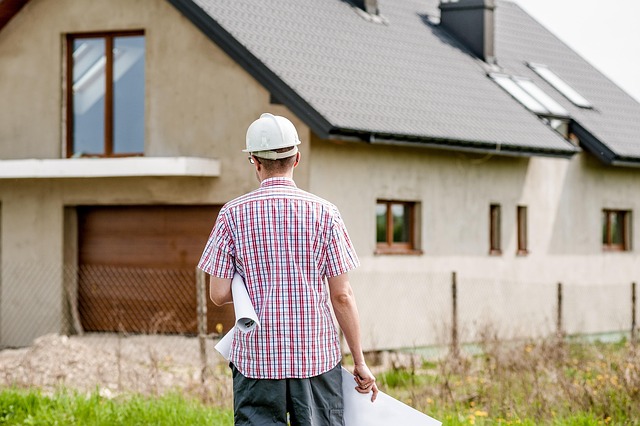 Haus im Rohbau. Im Vordergrund ein Bauleiter mit Plänen in der Hand.